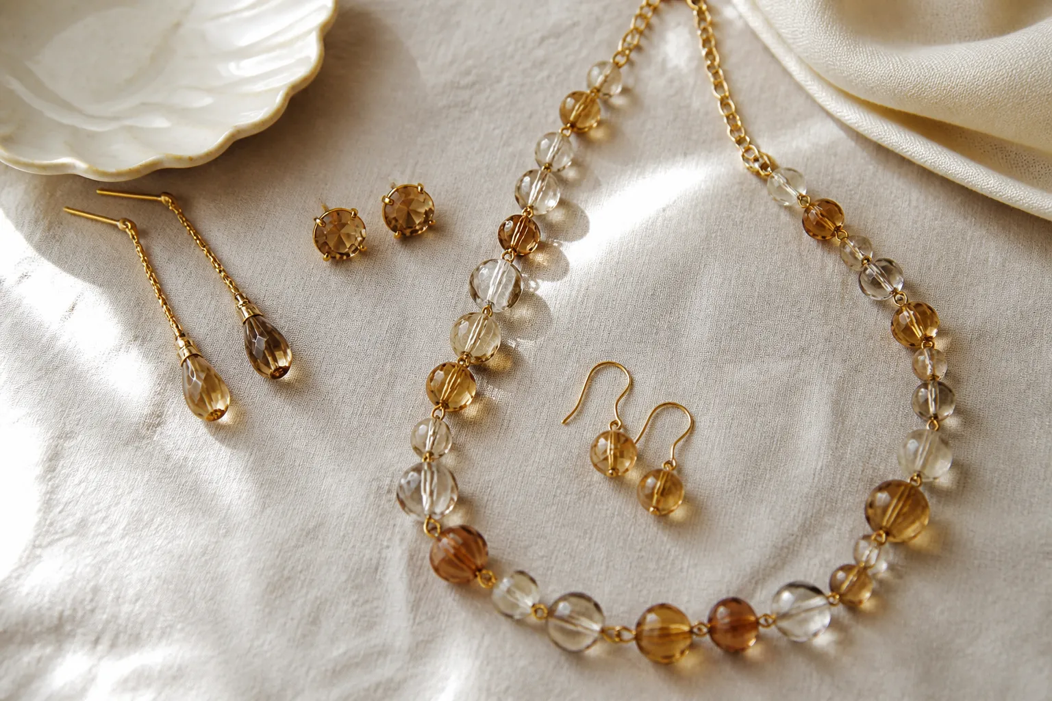 محل ذهب - Annotated product mockup showing a flat-lay of STRAND jewelry collection — drop earrings, rhinestone studs, two-tone glass bead necklace-and-earring set — arranged on a muted cream linen surface, soft natural window light from the left, product labels in Arabic pointing to key features like material and finish