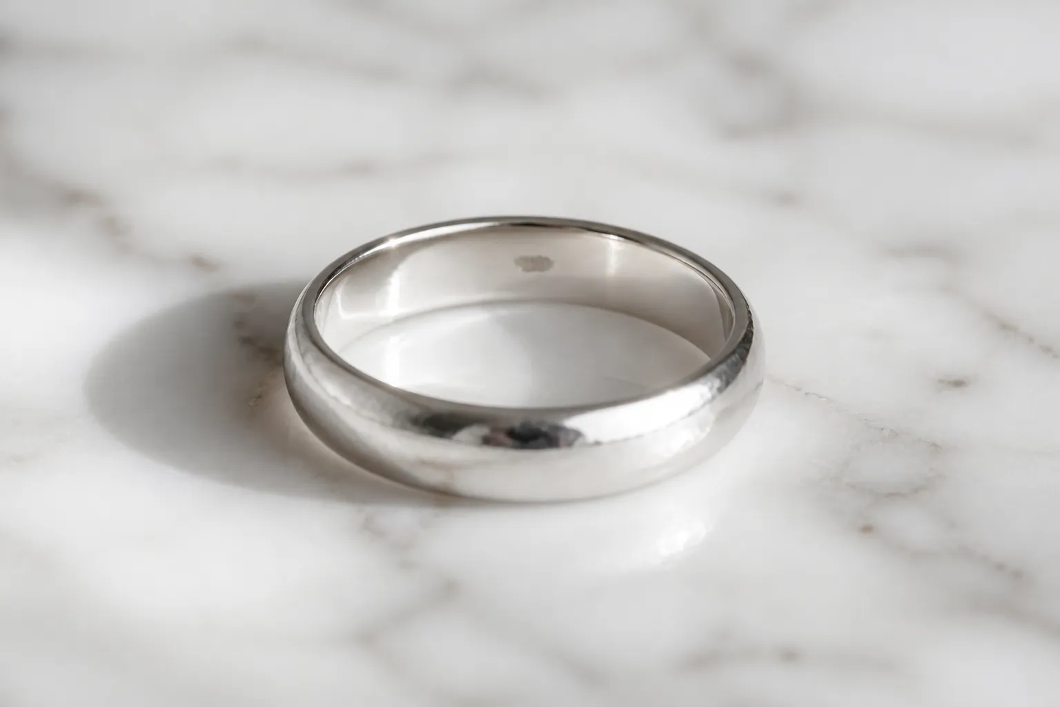 925 silver ring - Photorealistic close-up of an elegant 925 sterling silver ring on a textured white marble surface, showing the hallmark stamp "925" engraved on the inner band, natural studio lighting from the left, shallow depth of field with soft background blur, fine jewelry photography style
