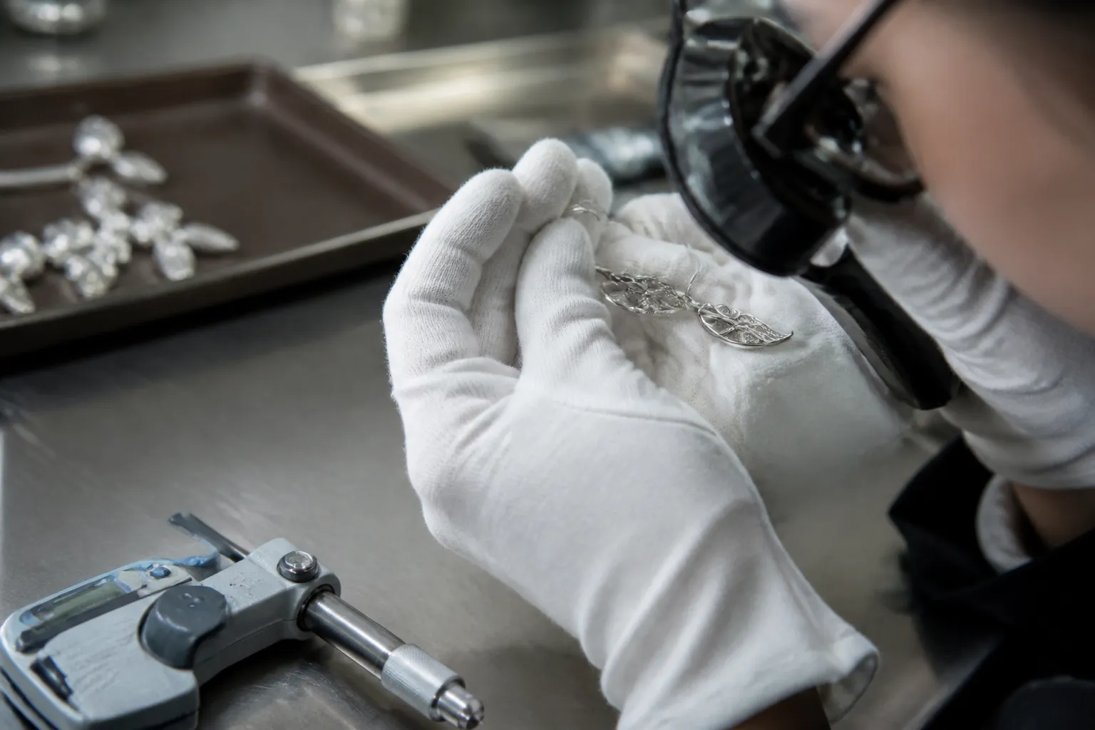 pendientes plata - Proceso de inspección de calidad en taller de joyería: técnico revisando pendientes plata bajo lupa con calibre de medición de grosor de recubrimiento visible en primer plano
