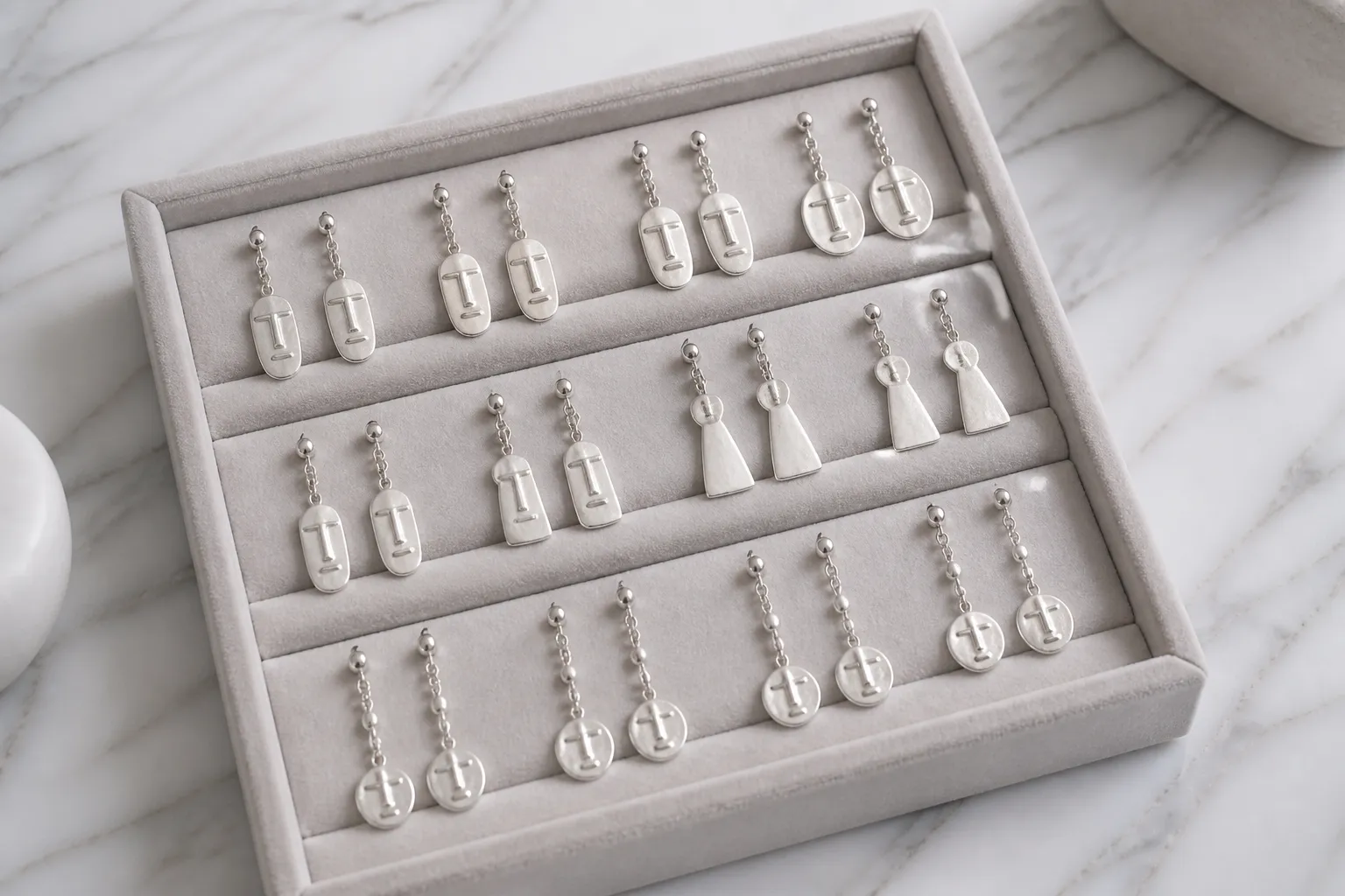 cyclade argent - Plateau de présentation de boucles d'oreilles pendantes finition argent d'inspiration cycladique, disposées sur fond de marbre blanc, style éditorial B2B