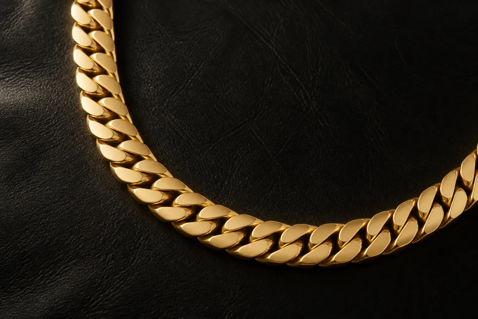 chaine en or homme - Vue rapprochée d'une chaîne en or jaune 18 carats pour homme, maillons gourmette larges, sur fond de cuir noir mat, lumière studio chaude