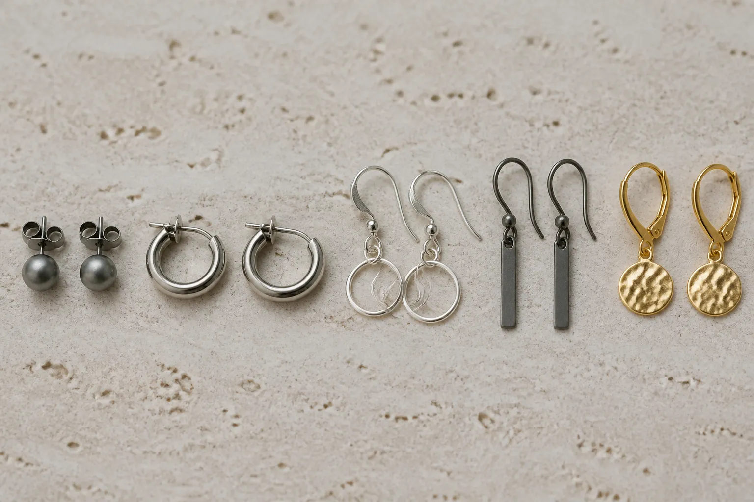 titan ohrringe - Vergleichsfoto verschiedener Ohrring-Materialien nebeneinander — Titan, Edelstahl, Sterling Silber, Niob und vergoldete Varianten auf neutralem Hintergrund mit Materialbeschriftungen
