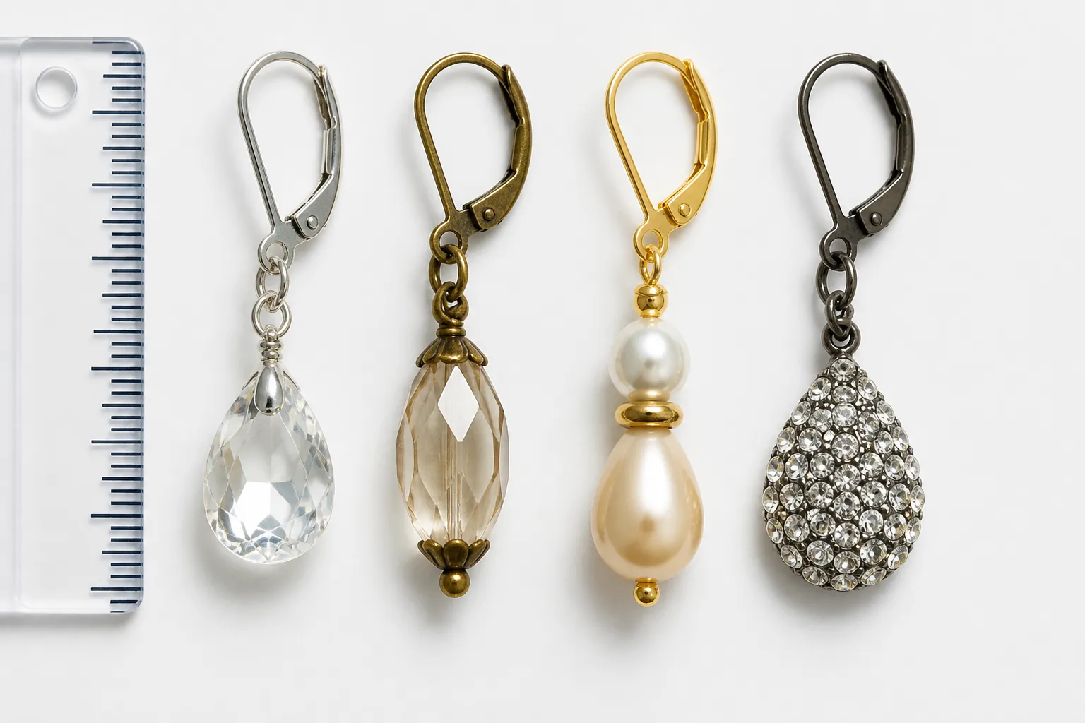 tropfen ohrringe - Nahaufnahme einer Flatlay-Komposition verschiedener Tropfen Ohrringe – Kristall, Vintage-Glas, zweifarbige Perlen, Strass – nebeneinander auf weißem Hintergrund mit Maßstabslineal, um Größen und Stilunterschiede zu veranschaulichen