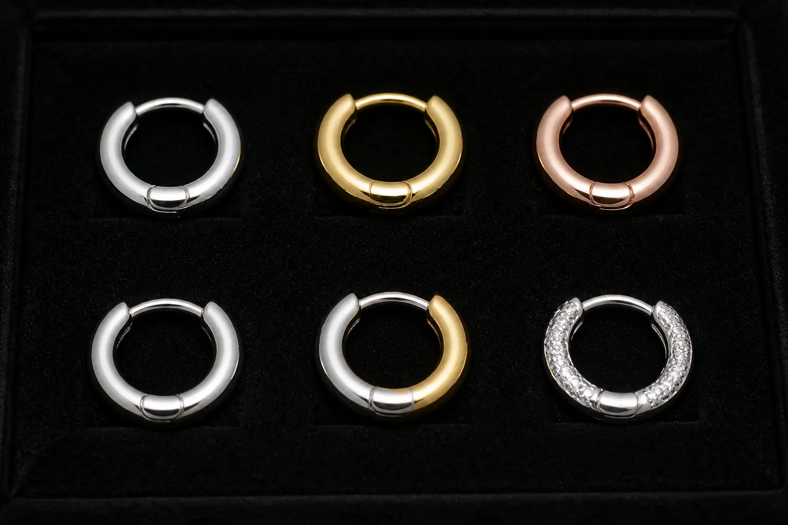 ohrringe creolen silber - Nahaufnahme einer Musterkarte mit sechs Creolen-Varianten (Silber, Gold, Roségold, Edelstahl, Bicolor, mit Zirkonia) auf schwarzem Samtuntergrund – typische OEM-Musteransicht für Großhandelseinkäufer