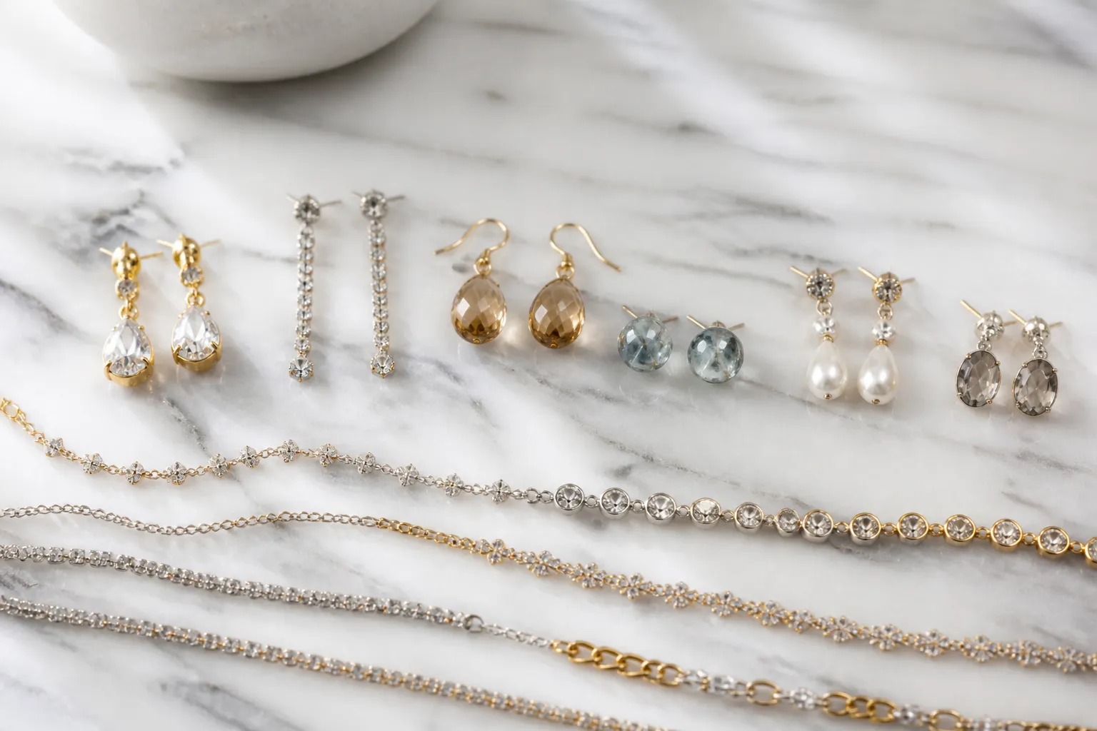 custom jewelry - Photorealistic editorial flat-lay of gold-plated drop earrings, rhinestone necklace sets, and glass bead studs arranged on a light marble surface — representing the type of stock catalog fashion jewelry available through OEM suppliers as a cost-effective alternative to fully custom jewelry production