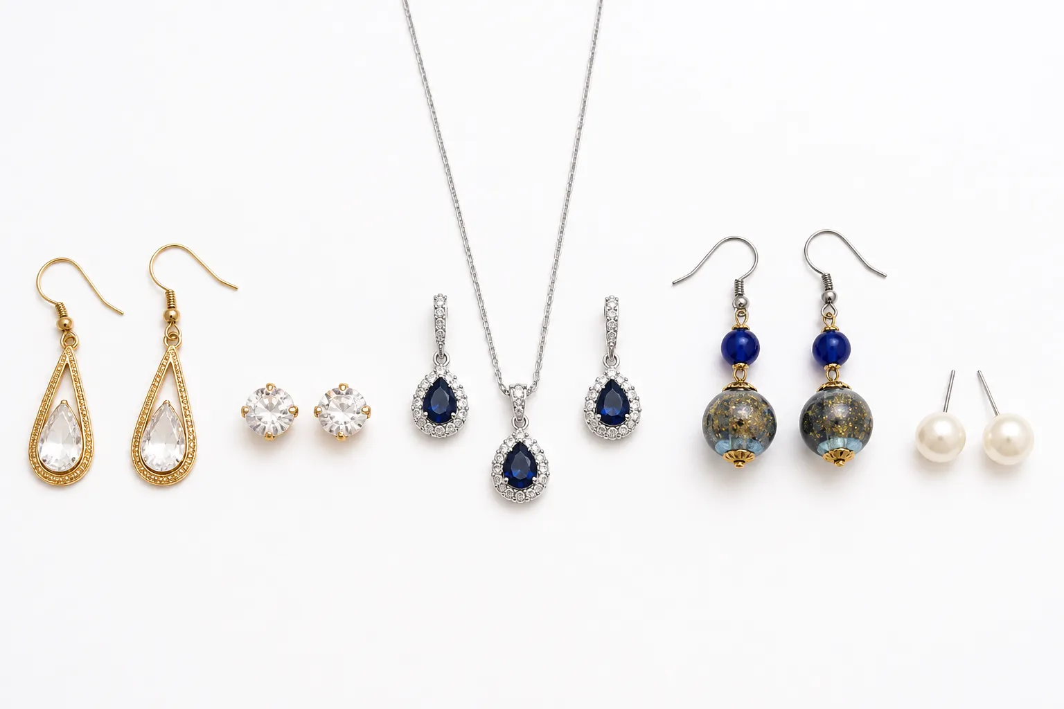 مجوهرات الاناقة - Annotated product flat-lay on a clean white surface showing five distinct jewelry pieces side by side: gold-plated drop earrings, rhinestone studs, a necklace-and-earring matching set, two-tone glass bead earrings, and a minimalist pearl stud — each piece labeled with a small callout tag naming its material, top-down angle, soft diffused studio lighting, no human hands, no decorative elements