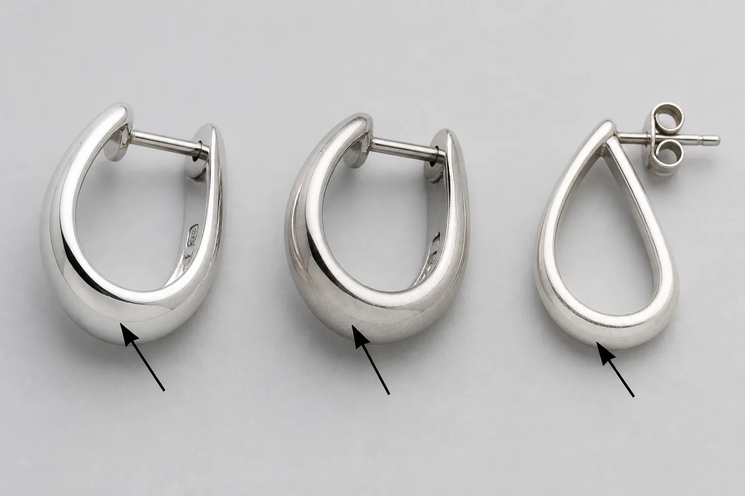 oro blanco - Comparativa fotorrealista sobre fondo neutro de tres piezas de joyería con etiquetas identificativas: un pendiente de oro blanco macizo de 18K con sello grabado visible, una pieza chapada en rodio sobre cobre y un pendiente de plata 925, con flechas que señalan las diferencias de tono y acabado superficial