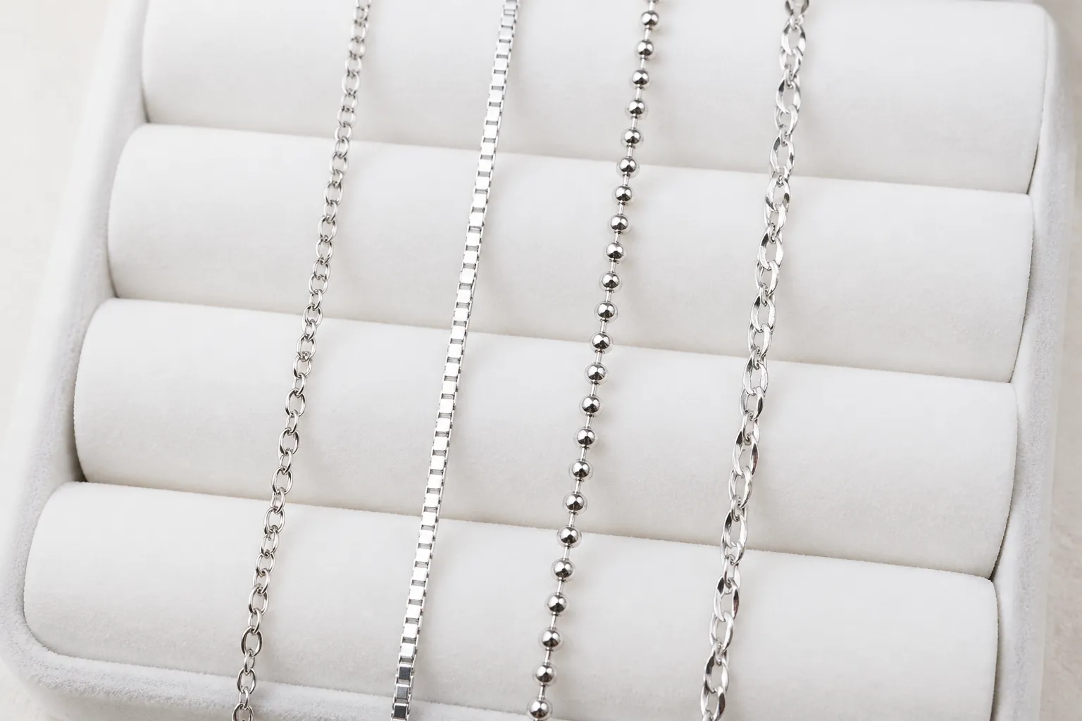 silberkette damen - Nahaufnahme verschiedener Damenketten-Stile auf einem weißen Schmuckdisplay – Ankerkette, Venezianerkette, Kugelkette und Singapurkette in Silber, mit Materialbeschriftung 925 Sterling Silver und rhodiniertes Kupfer nebeneinander zum Vergleich