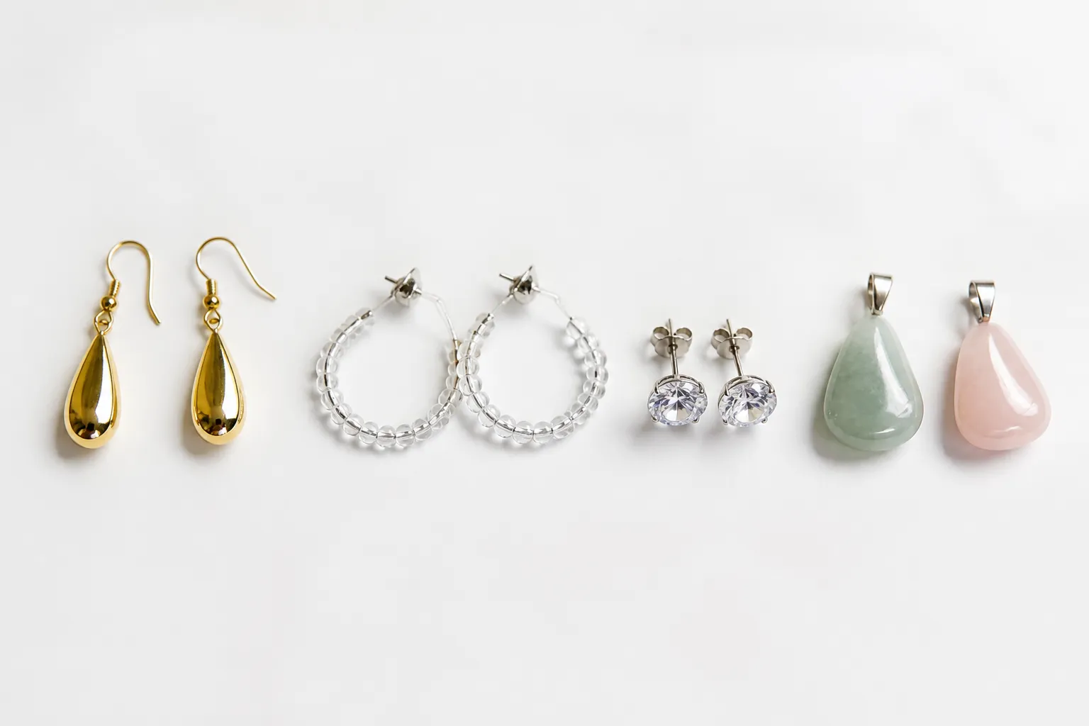 silberschmuck - Flachbild-Aufnahme verschiedener Alternativen zu Silberschmuck nebeneinander – vergoldete Tropfenohrringe, Glasperlen-Creolen, rhodinierte Strass-Stecker und Naturstein-Anhänger auf weißem Studiohintergrund, mit Preisetiketten für Händlervergleich