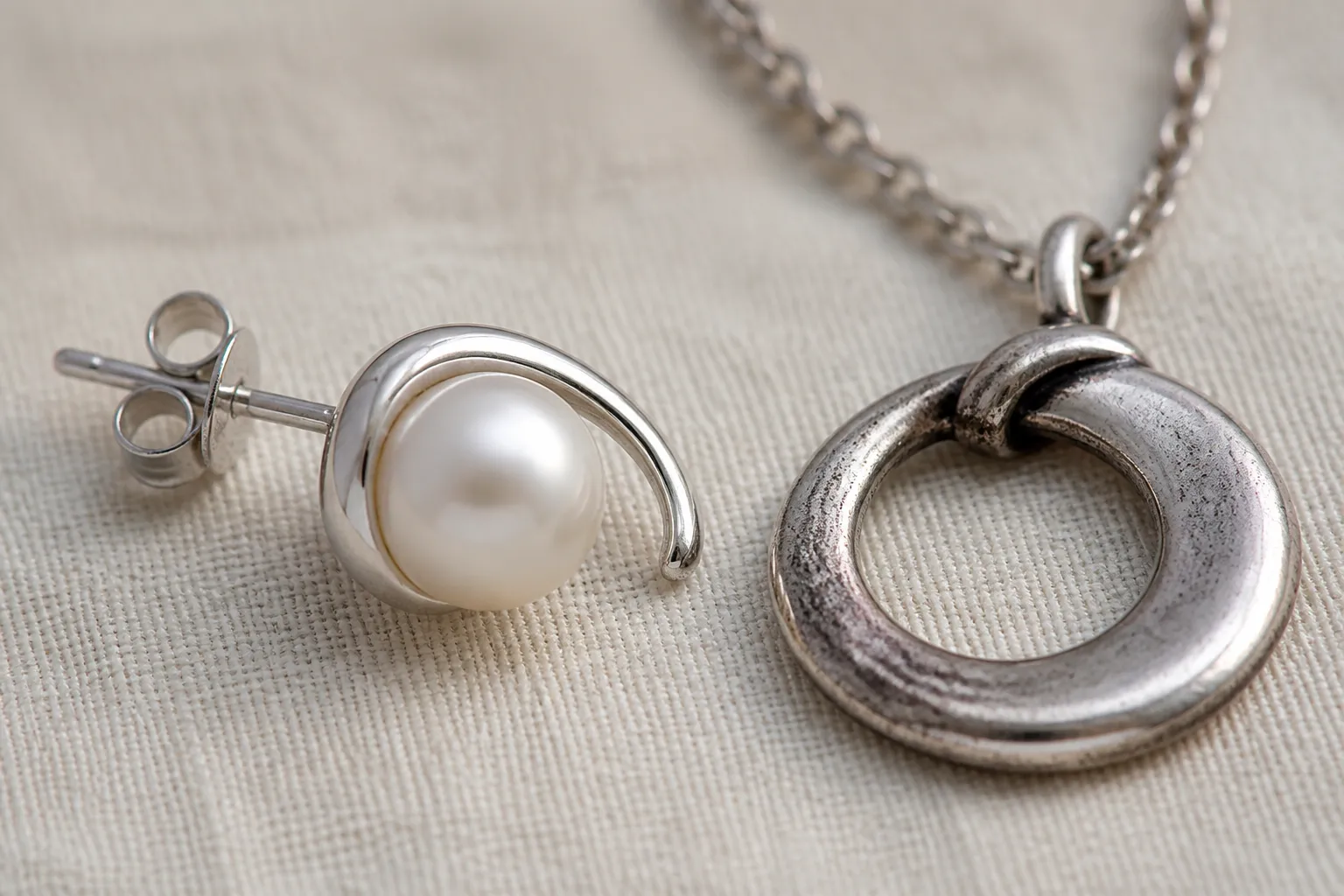 silber - Detailaufnahme eines rhodium-plattierten Perlen-Ohrrings neben einem 925er Silber-Pendant — Bildunterschrift erklärt die optischen Unterschiede und die unterschiedliche Anlaufeigenschaft nach 6 Monaten