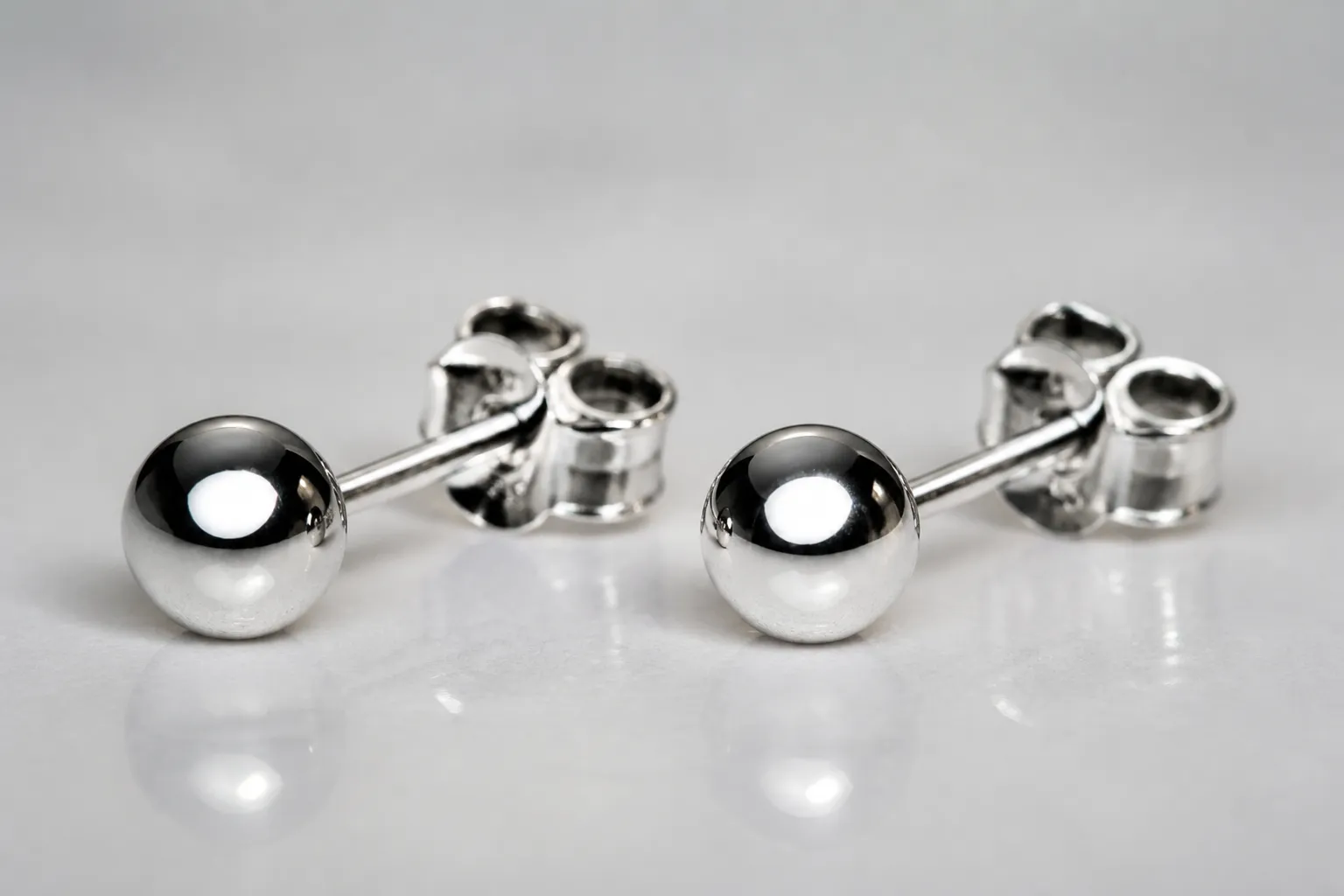 ohrstecker silber - Nahaufnahme eines rhodinierten Kupfer-Ohrsteckers neben einem 925er Silber-Referenzstück unter professioneller Studioausleuchtung, um die visuelle Ähnlichkeit der Oberflächenveredelung für Einkäufer demonstrierbar zu machen