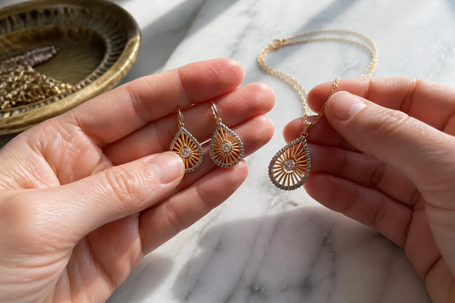 must have brand jewelry - Photorealistic close-up of a buyer's hands examining a Two-Tone Sunburst Teardrop Earrings & Necklace Set-Gold — STRAND (ستراند) on a white marble surface, natural window lighting highlighting the metal texture and glass clarity, shallow depth of field, documentary style