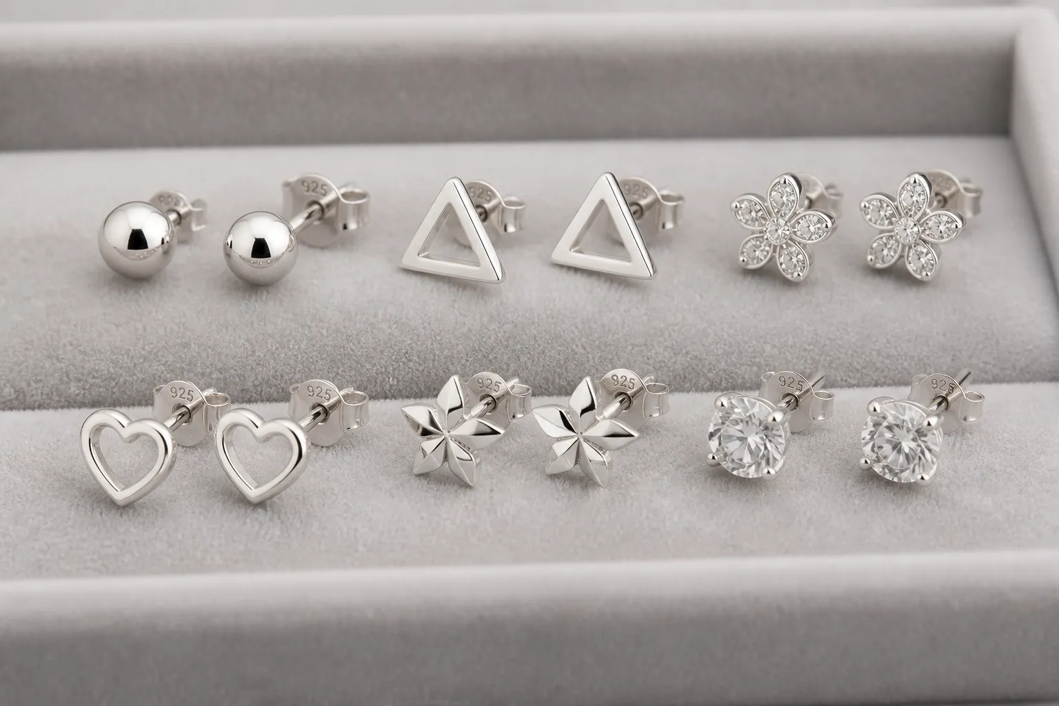 ohrstecker silber - Nahaufnahme mehrerer 925er Sterling-Silber-Ohrstecker auf einem grauen Velours-Tablett mit sichtbaren Hallmark-Prüfstempeln und unterschiedlichen Ohrstecker-Formen – sachliches Produktfoto für Einkäufer
