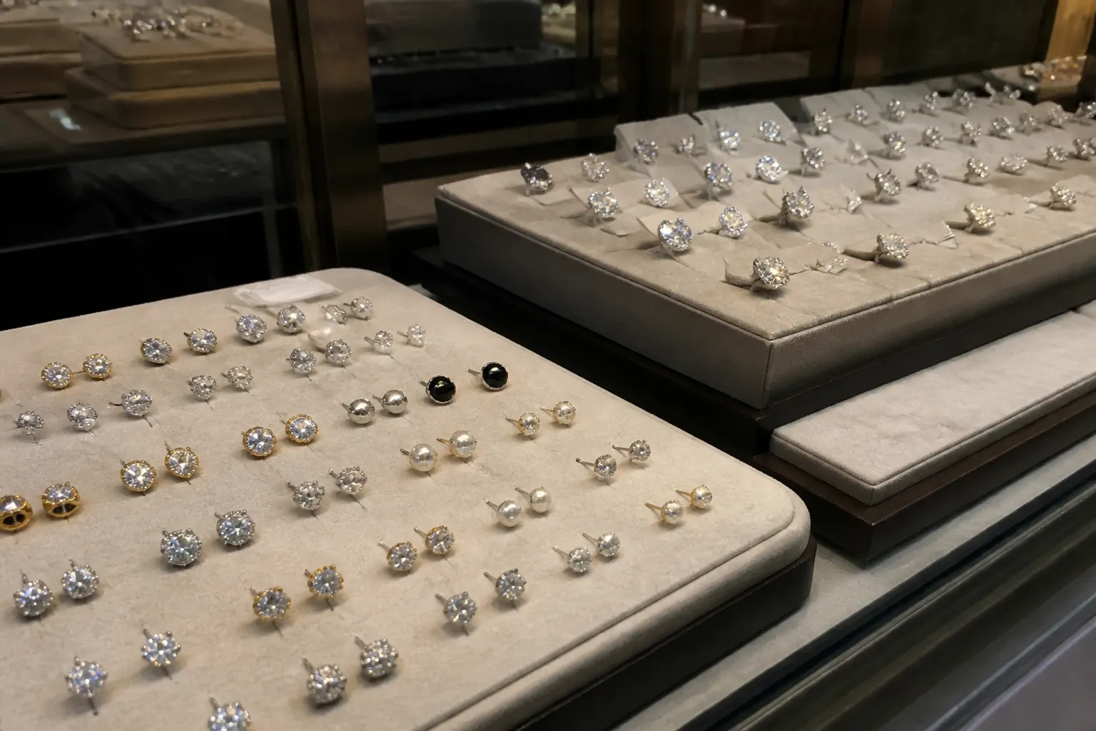 ohrstecker silber - Beispielfoto einer Ladentheke mit gemischtem Ohrstecker-Sortiment: rhodinierte Modeschmuck-Ohrstecker vorne im Einstiegspreissegment, 925er Silber-Ohrstecker im hinteren Premium-Bereich mit unterschiedlichen Preisetiketten – realitätsnahe Einzelhandelsumgebung für Vergleichszwecke