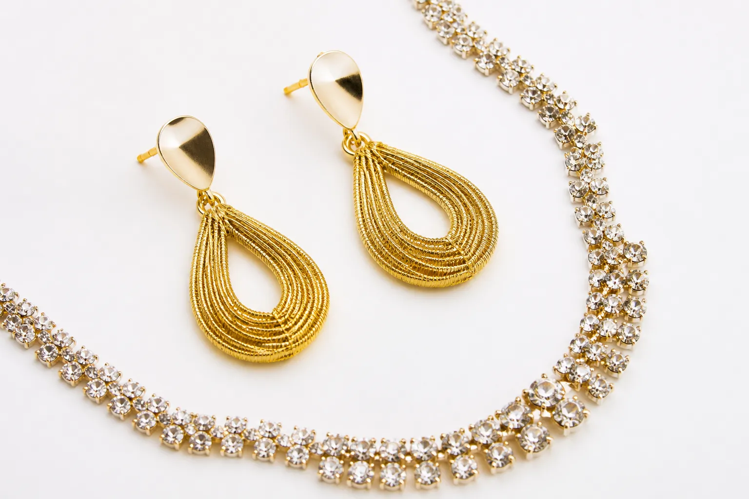 custom jewelry - Flat-lay product photo of STRAND's gold-plated copper drop earrings and rhinestone necklace set against a clean white background, showing finish quality at the SKU level