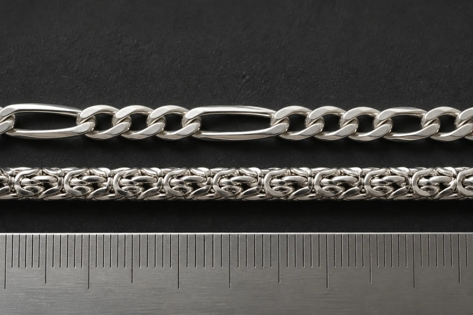 königskette silber - Nahaufnahme einer Figaro-Kette und einer Königskette nebeneinander auf schwarzem Schmuckpad – deutlich sichtbares unterschiedliches Gliedermuster mit Maßstab-Lineal