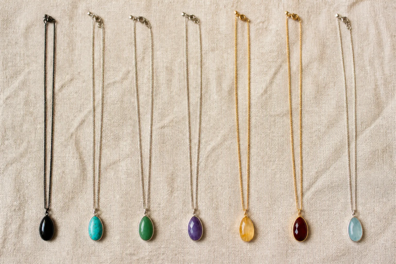 collar con piedra natural - Fotografía plana (flat lay) fotorrealista de siete collares con piedra natural dispuestos en fila sobre superficie de lino beige — onix negro, turquesa azul verdosa, jade verde, amatista violeta, citrino dorado, granate rojo oscuro y aguamarina celeste — cadenas metálicas desplegadas, iluminación lateral natural de estudio sin sombras duras, sin accesorios adicionales