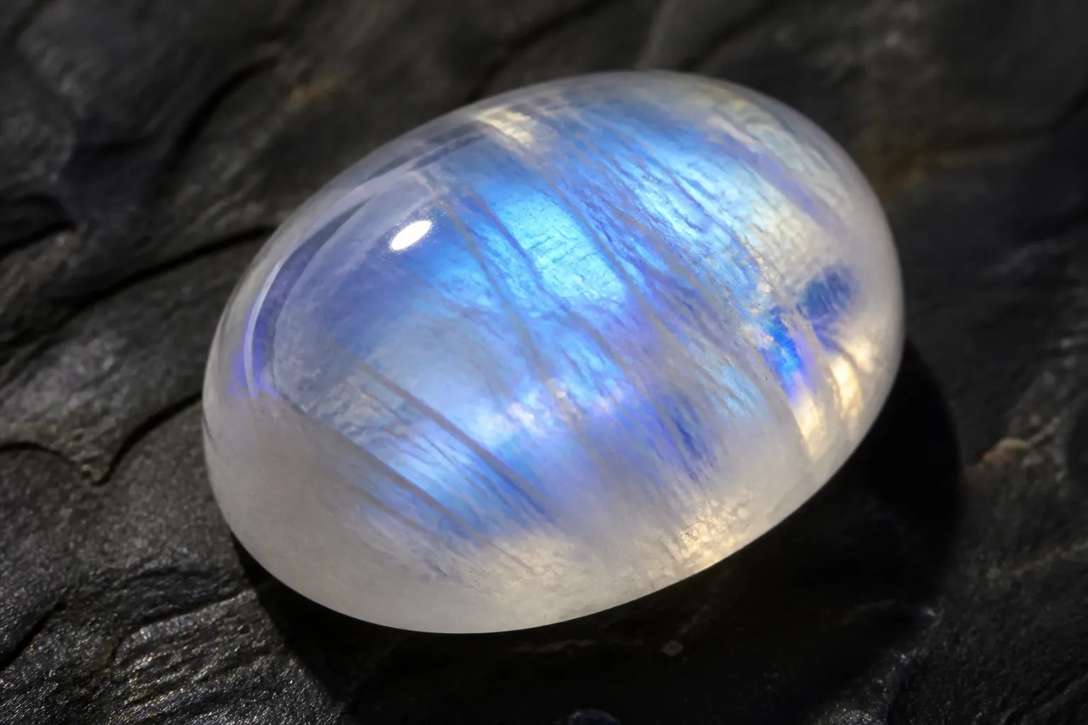 pierre de lune - Photographie en gros plan d'une pierre de lune polie cabochon montrant l'effet d'adularescence — reflets bleutés et argentés glissant sur la surface translucide sous différents angles d'éclairage
