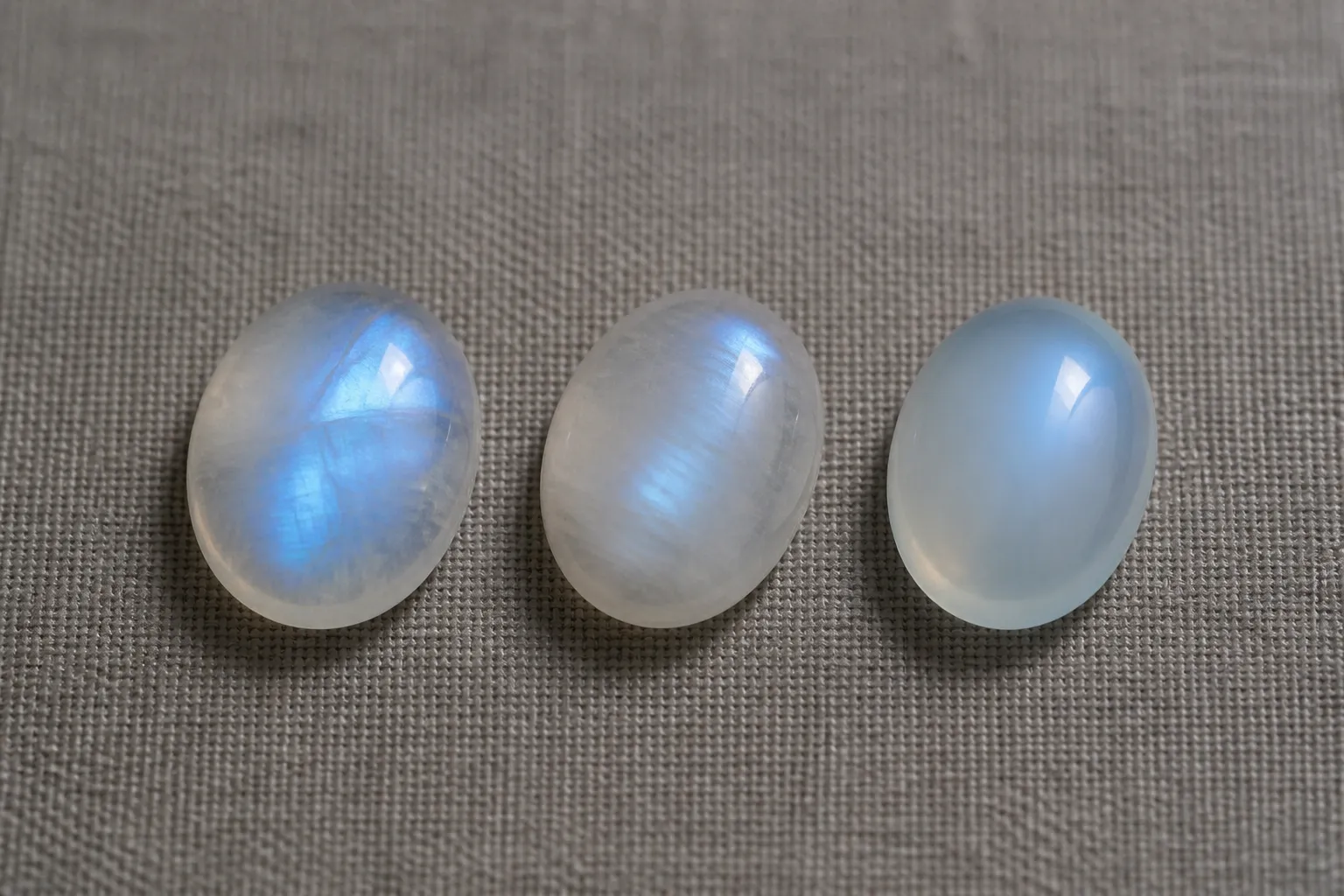 pierre de lune - Comparaison visuelle côte à côte entre une pierre de lune naturelle avec adularescence bleue (grade A), une pierre de lune reconstituée (grade B) et une imitation en verre bleu laiteux — guide d'identification pour les acheteurs professionnels