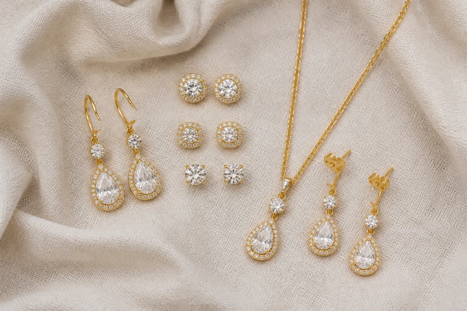 كيف اتاجر من الصين - Annotated product mockup showing a flat-lay arrangement of gold-plated drop earrings, rhinestone stud earrings, and a necklace-earring set on a cream linen fabric background, each piece labeled with material tags in Arabic and English, soft diffused studio lighting, top-down composition