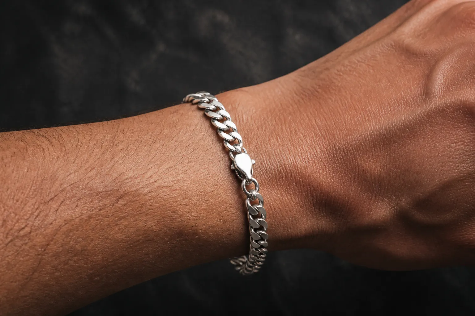 männer armband silber - Photorealistisches Editorial-Foto eines 925er Sterlingsilber Kettenarmbands am Männerhandgelenk, mit sichtbarer Flachpanzer-Struktur und Karabinerverschluss auf dunklem Untergrund