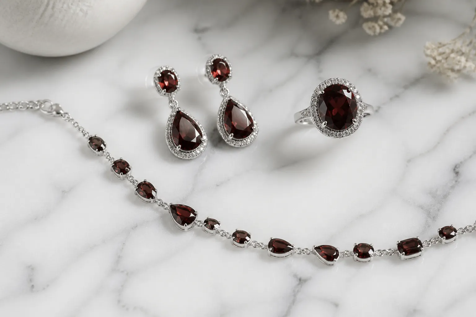 piedra granate - Foto editorial de una selección de joyas con piedra granate — pendientes, anillo y pulsera — dispuestos sobre mármol blanco, ilustrando la variedad de formatos disponibles y la combinación con plata
