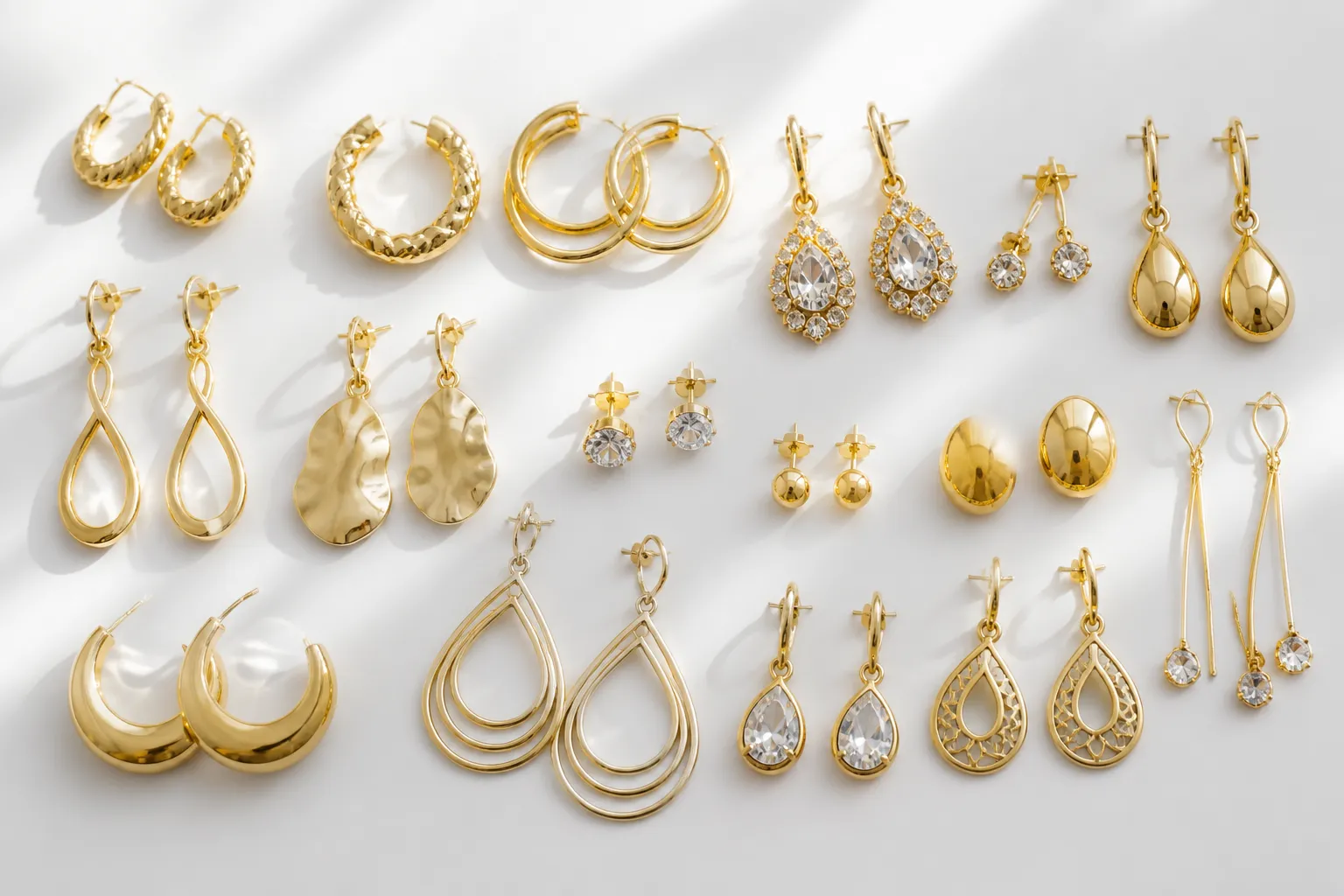 حكم شراء المطلي بالذهب من الإنترنت - Annotated product mockup showing a flat-lay of gold-plated copper earring styles from a wholesale catalog — drop earrings, stud earrings, rhinestone designs arranged on a white surface, with small material labels indicating "copper base + gold plating" in Arabic, soft natural top-down light, clean editorial composition