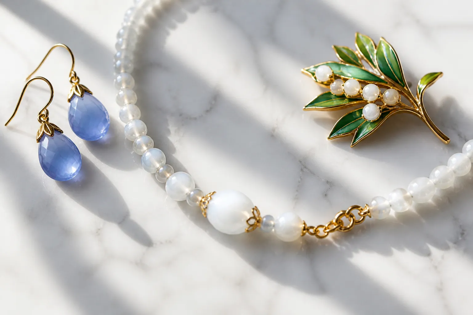 calcedonia piedra - Flatlay de joyería de moda mostrando aretes colgantes de calcedonia azul, un collar de cuentas de calcedonia blanca y un broche con piedra verde esmaltada, sobre superficie de mármol blanco con luz natural lateral