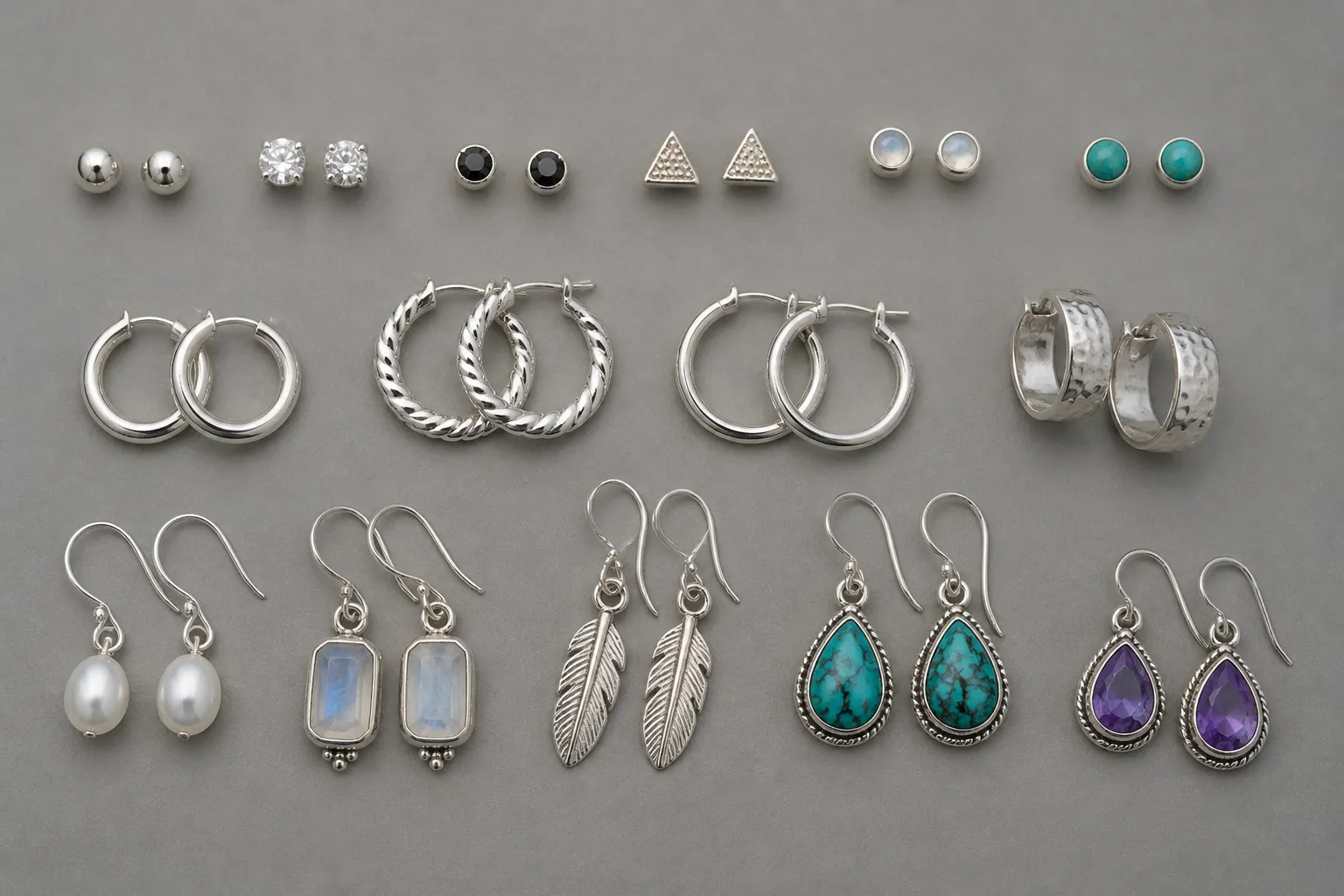 ohrringe silber 925 - Flatlay einer kuratierten Auswahl silberner 925-Ohrringe in verschiedenen Stilkategorien – Stecker, Creolen, Hänger mit Natursteinen – auf grauem Hintergrund mit Beschriftungspfeilen zu den jeweiligen Stiltypen