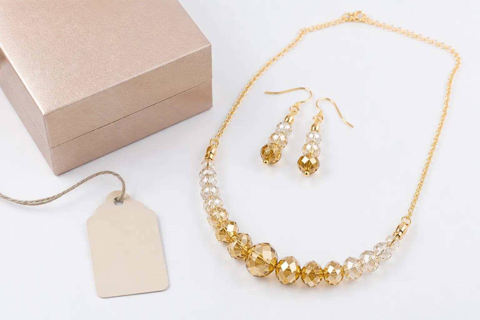 joyería relojería - Foto de producto sobre fondo blanco: set de collar y pendientes colgantes en cristal degradado con chapado en oro sobre cobre, junto a packaging de marca personalizada y etiqueta OEM, representando un pedido terminado listo para distribución DTC en mercados europeos.