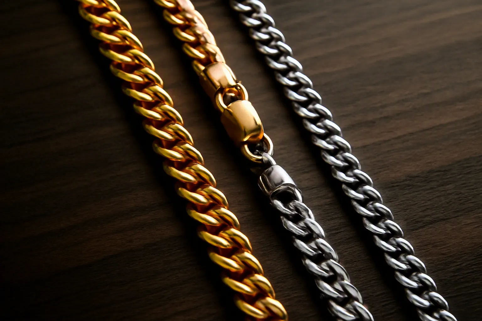 collier homme - Photo éditoriale comparant un collier homme plaqué or de style cubain et un collier en argent sterling — détail de la chaîne et du fermoir sur une surface en bois sombre, éclairage latéral pour faire ressortir les finitions