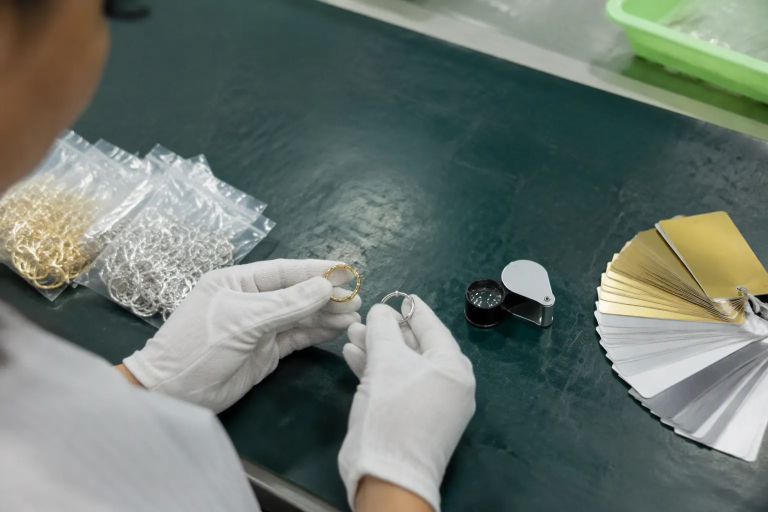 silberschmuck großhandel - Fotorealistisches Bild eines Mustervergleichs auf einem professionellen QC-Prüftisch – vergoldete und rhodinierte Kupferohrringe nebeneinander mit Farbkarten und Lupe, wie in einer chinesischen Schmuckwerkstatt bei einer Qualitätskontrolle vor dem Versand