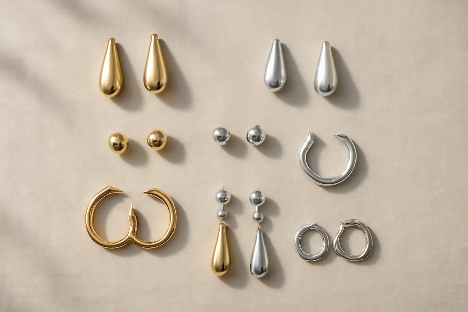 custom jewelry - Editorial flat lay photograph of diverse earring styles including drop, stud, and hoop designs in gold and rhodium finishes arranged on a neutral background, demonstrating the range of customizable OEM fashion jewelry options