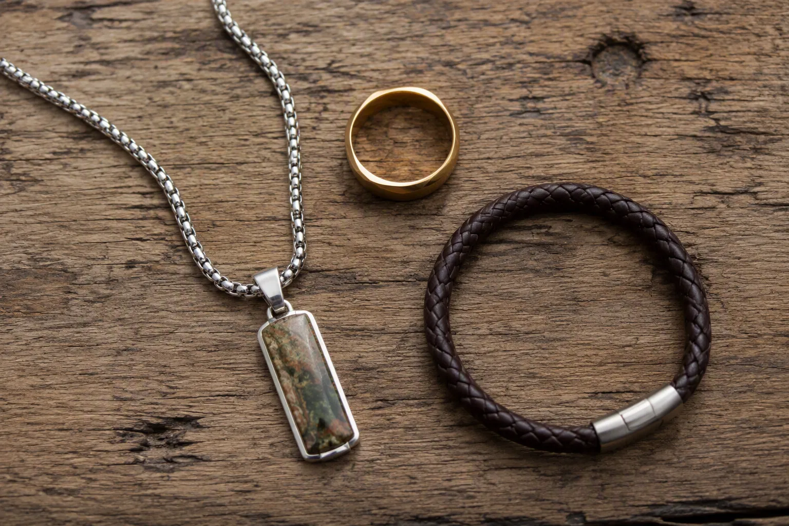 modeschmuck herren - Editoriales Produktfoto: Herren-Modeschmuck-Kollektion auf Holzuntergrund – Kette mit Naturstein-Anhänger, schlichter vergoldeter Ring und Lederarmband, Lifestyle-Setting für DTC-Shop-Produktbilder