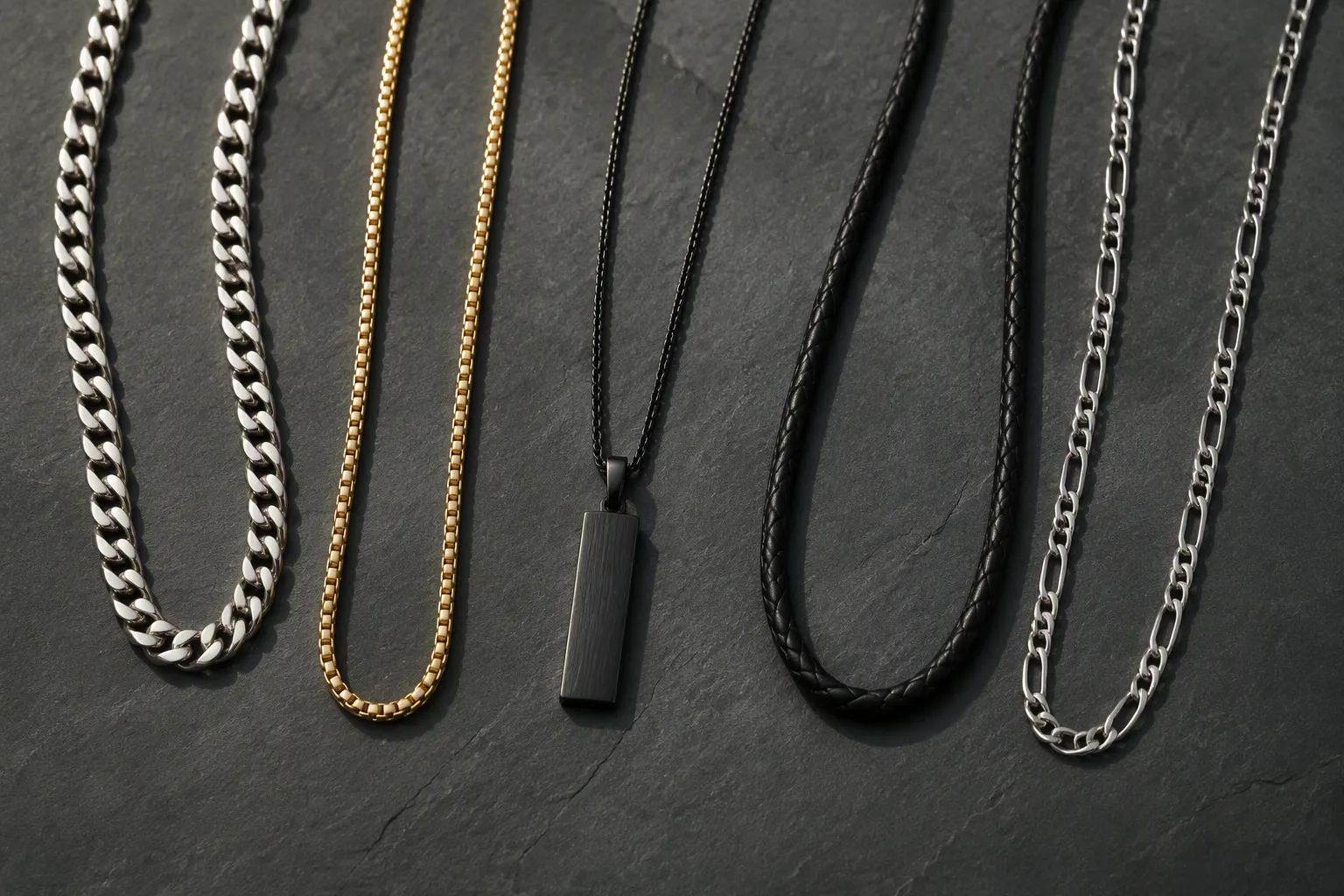 cheap guy necklaces - Photorealistic flat-lay of five men's necklaces arranged on a dark matte surface — chain links, pendants, and cord styles — various metal tones, natural side lighting casting soft shadows, overhead product photography style