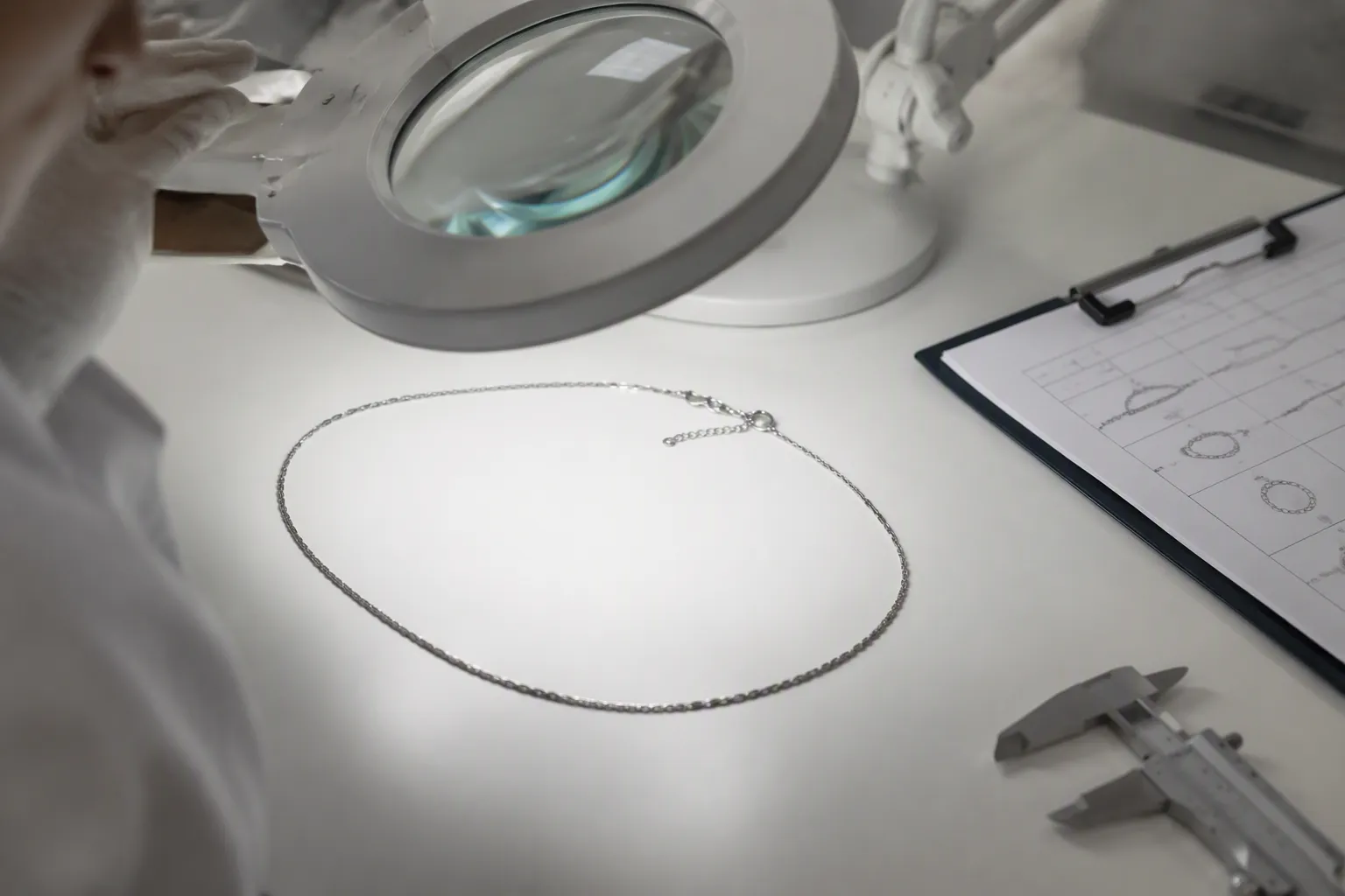 schmuck kette - Editorial photo of a QC inspection workstation showing rhodium-plated necklace chains being examined under magnification, with a checklist and measurement tools visible — representing in-house quality control before shipment