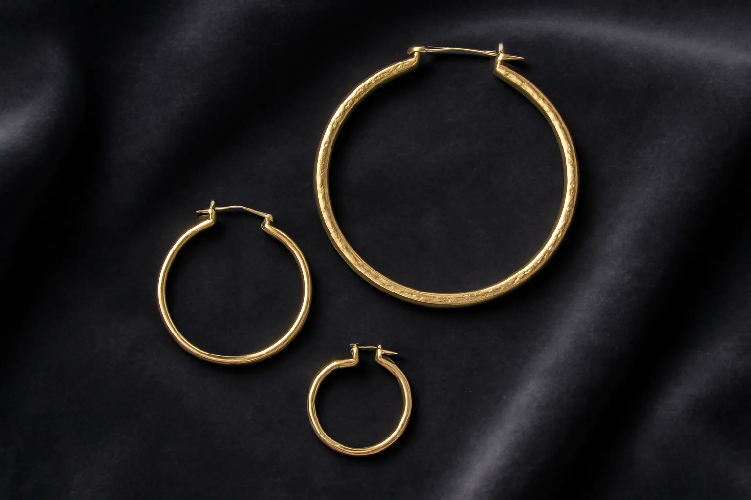 pendientes de aro de oro - Selección editorial de pendientes de aro de oro dorados en diferentes diámetros — 10 mm, 25 mm y 50 mm — sobre superficie de terciopelo oscuro, mostrando variaciones de grosor del aro, acabado liso y acabado texturizado
