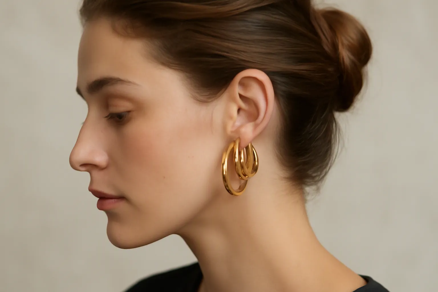pendientes de aro de oro - Foto editorial de pendientes de aro de oro dorados usados por una mujer con pelo recogido, mostrando cómo caen aros de distinto tamaño en el lóbulo, sobre fondo neutro de estudio con iluminación natural