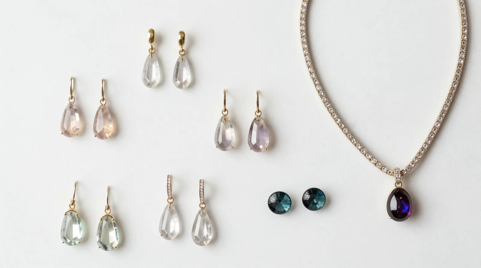 bijoux originaux - Flat lay photographique de boucles d'oreilles pendantes en cristal gradient, sets collier-strass et studs en verre bicolore disposés sur fond marbre blanc — illustrant la diversité stylistique d'un catalogue bijoux originaux cross-border