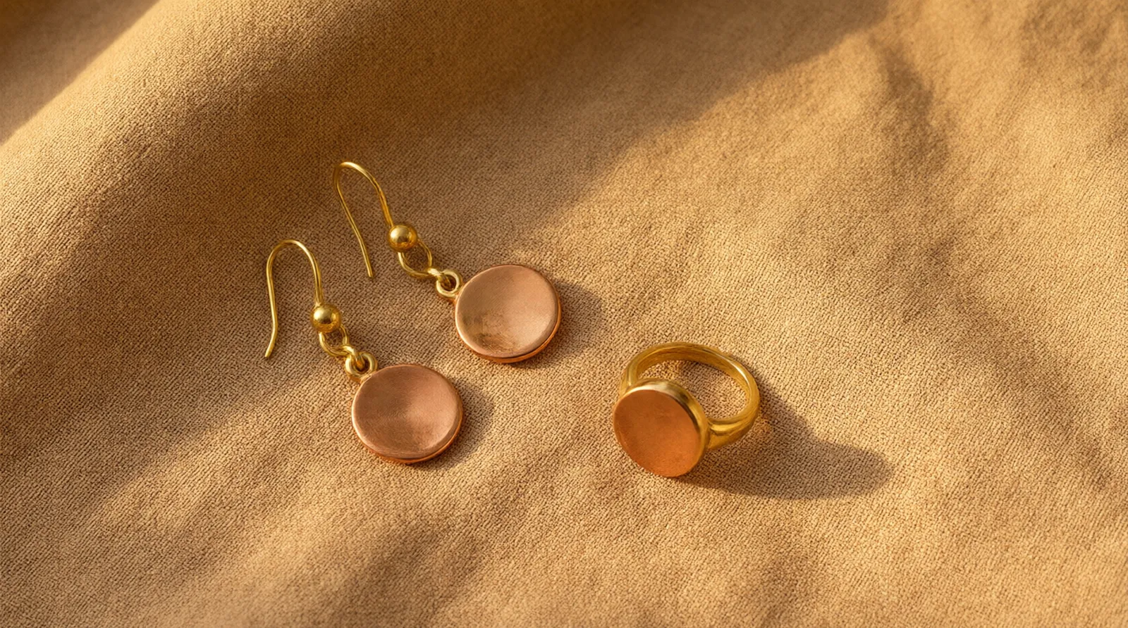bijoux en cuivre - Photo éditoriale de boucles d'oreilles pendantes et d'une bague en cuivre plaqué or sur fond de tissu texturé — style flat lay pour boutique en ligne française, lumière chaude