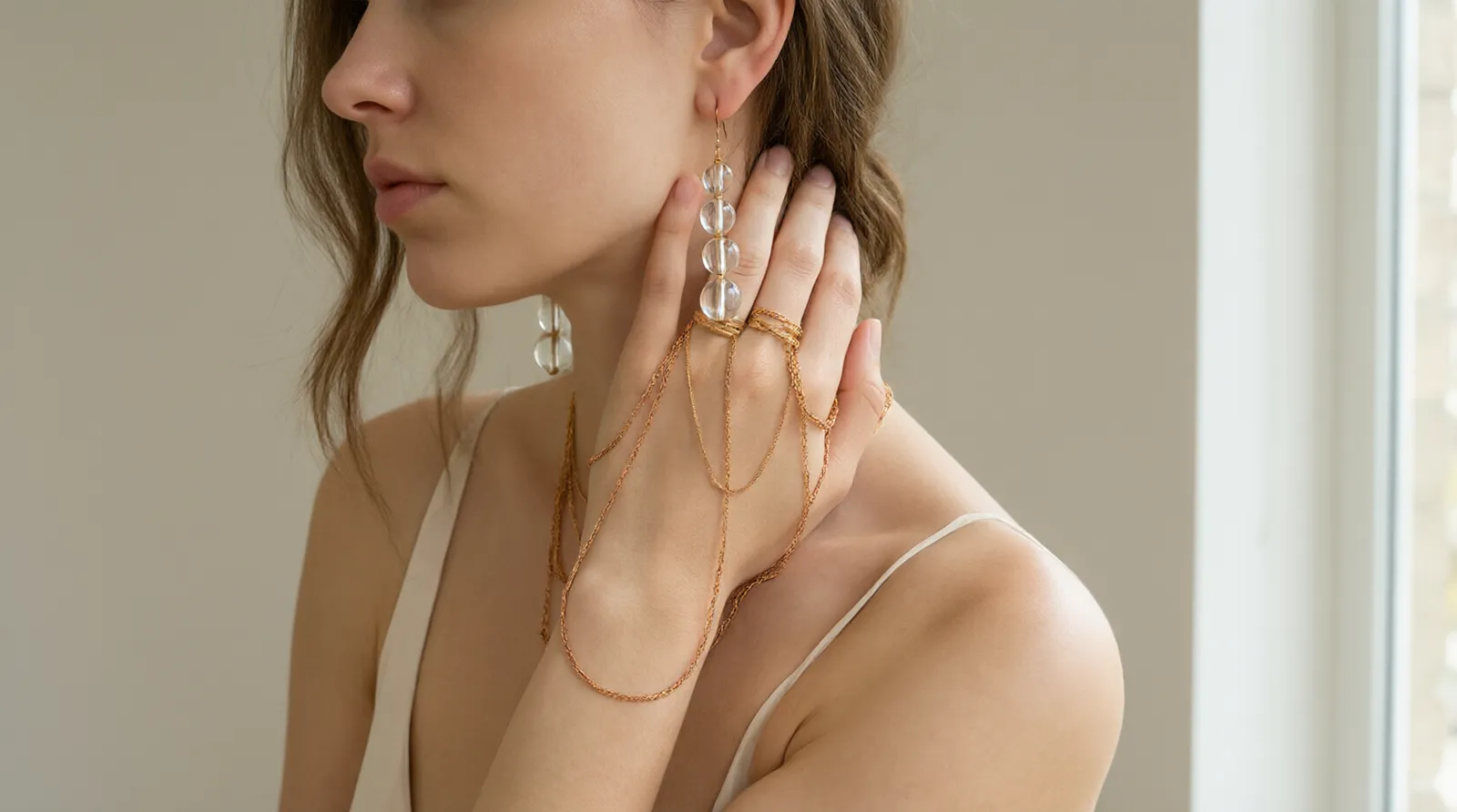 designer modeschmuck - Editorial-Foto einer Modelhand, die mehrere Layer-Ketten und Statement-Ohrringe aus vergoldetem Kupfer und Glasperlen trägt, gestylt für einen modernen DTC-Onlineshop