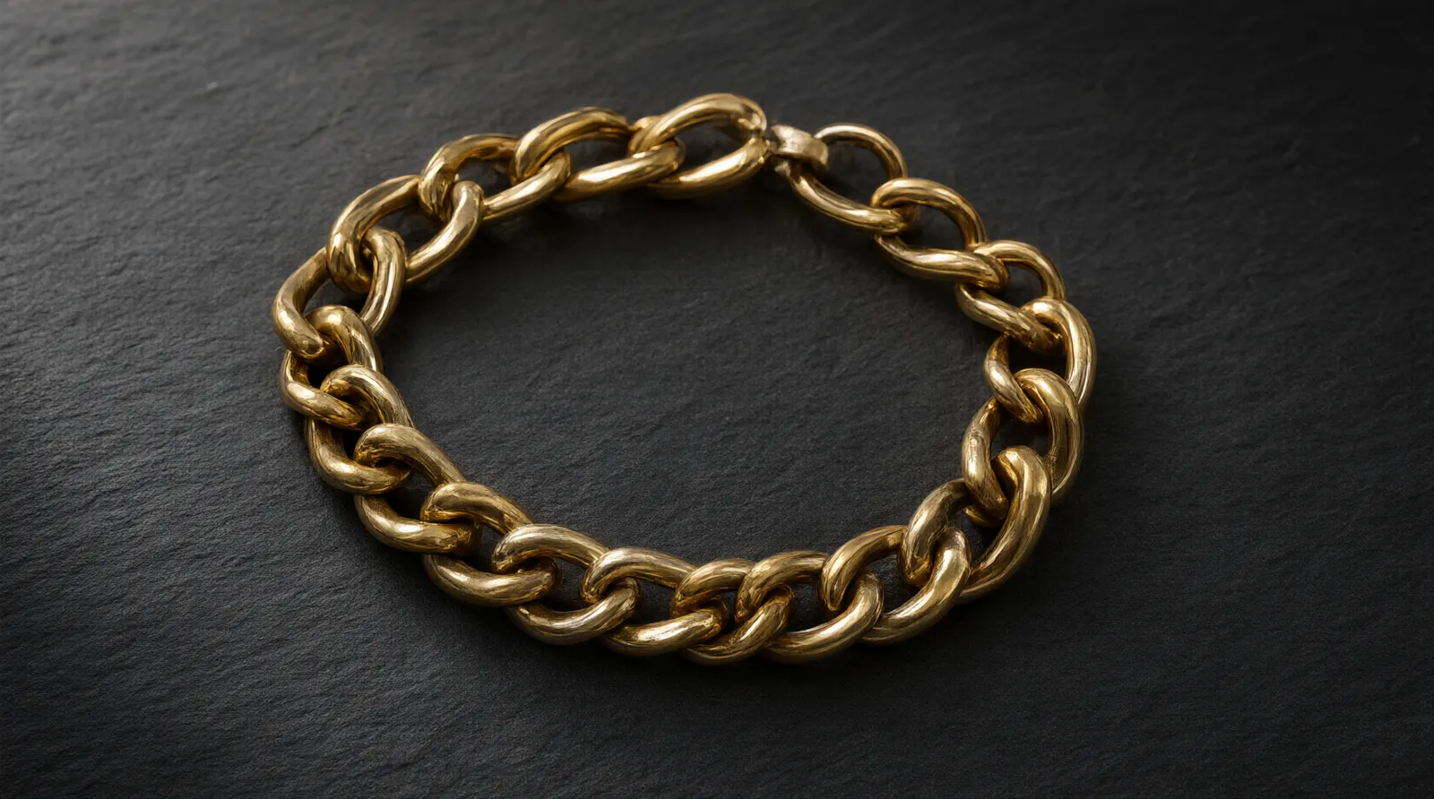 what is pvd gold - Photorealistic close-up macro shot of a polished stainless steel chain bracelet with a warm 18k PVD gold tone resting on dark slate, natural directional window light highlighting the uniform metallic sheen and smooth links, documentary product photography style